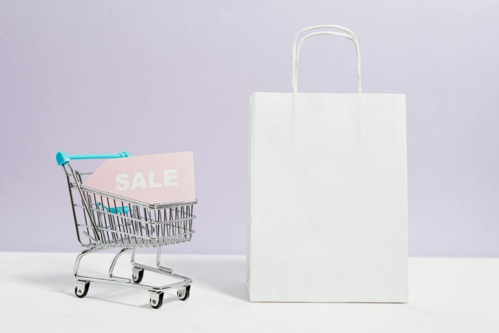 A miniature shopping cart with a sale sign beside a paper bag, perfect for online shopping themes.